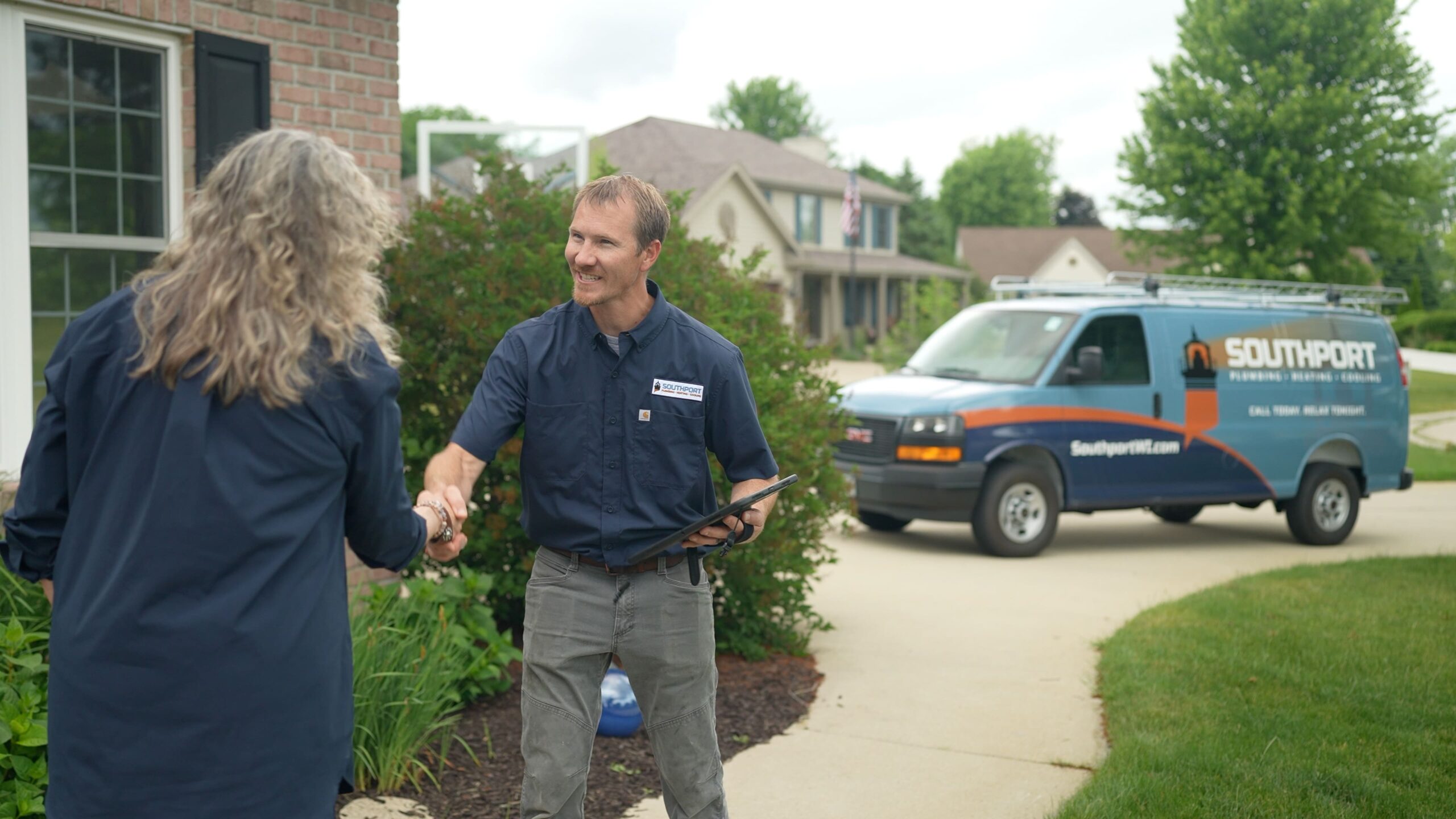 Two workers shake hands outside a suburban home, with a Southport service van in the driveway behind them.
