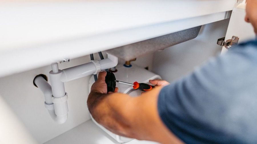 plumber clearing a drain line under a sink