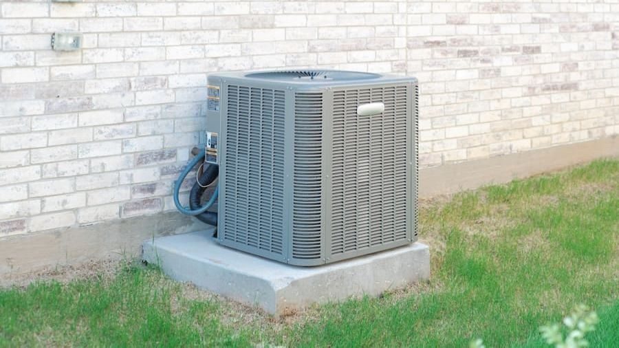 Outdoor central air conditioning condenser on a concrete pad beside a brick wall.