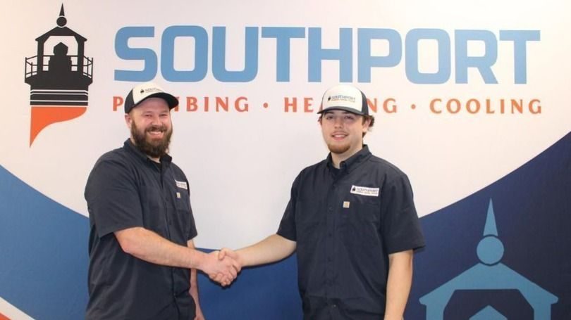Two service technicians in dark uniforms shake hands in front of a Southport sign that reads 'Piping • Heating • Cooling'.
