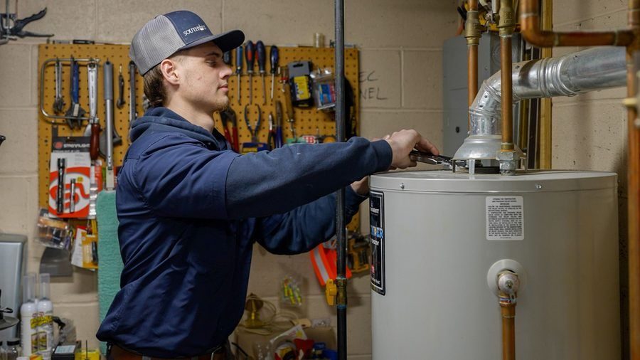 Young man in a cap and hoodie adjusting a water heater in a workshop garage setting