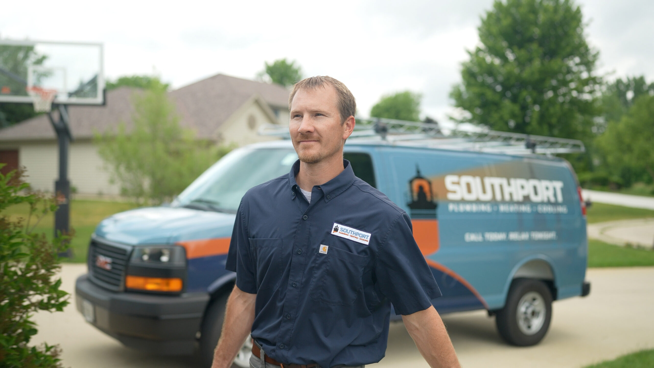 Man in a navy Southport uniform stands in a driveway with a blue service van and ladder rack in the background.