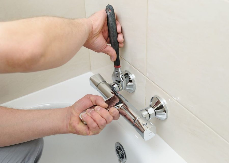 Plumber installing bathtub faucet and tightening it with wrench