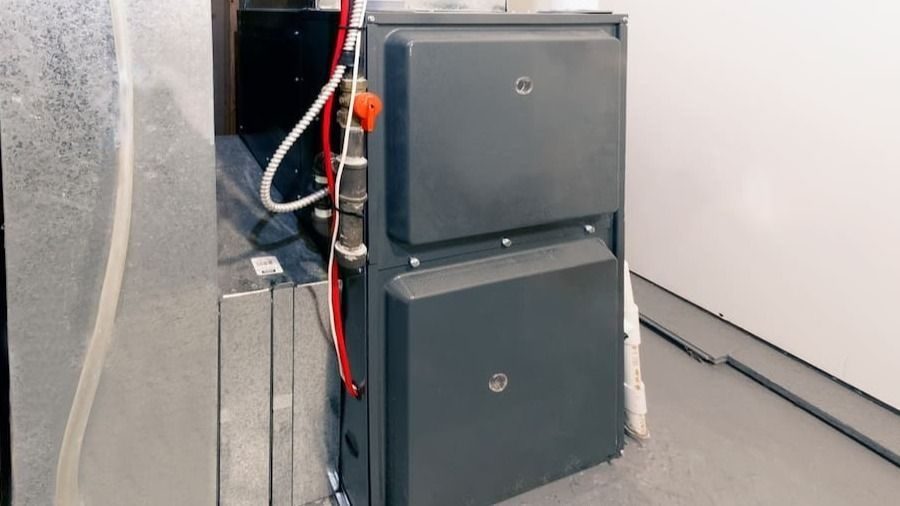 Two gray industrial furnace units in a mechanical room with red and white cables and ductwork nearby (indoor HVAC equipment). In-use look with metal panels and wiring exposed.